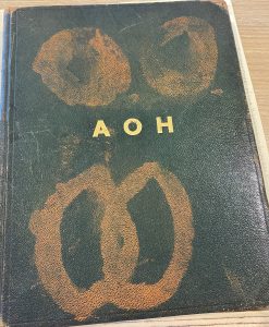 The cover of the A.O.H. scrapbook with the letters printed on it and four large letter "o"s that have been drawn on in orange paint as graffiti by the Orangemen.