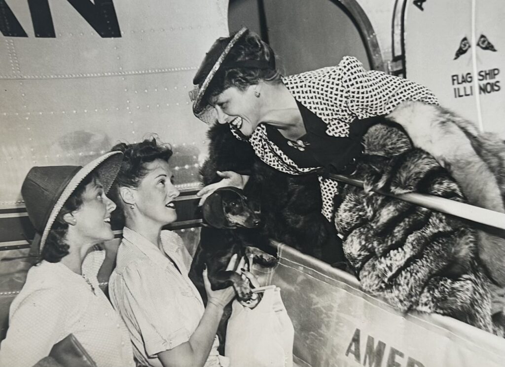 Black and white photo of Irene Rich, dressed in Hollywood glamour, smiling down at Frances and an unidentified woman from the door of an airplane