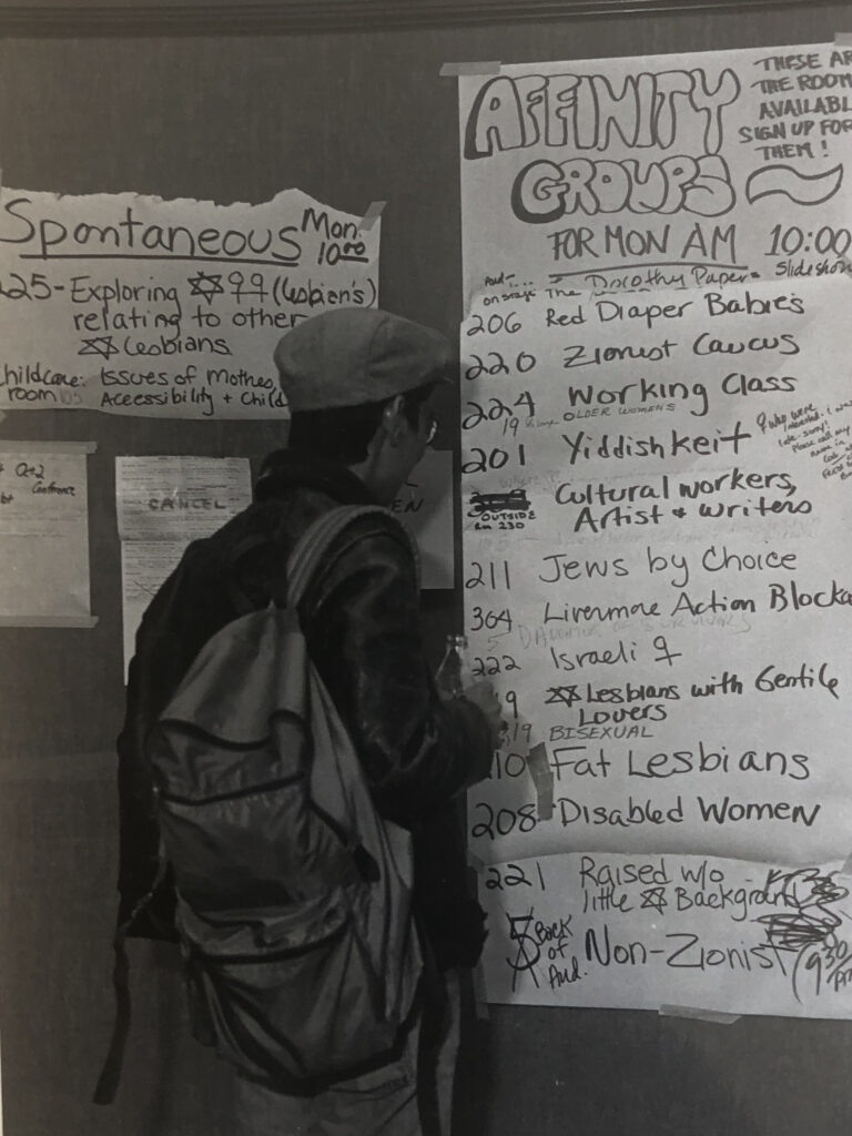 A person stands with their back to the camera reading a posted list of affinity groups.