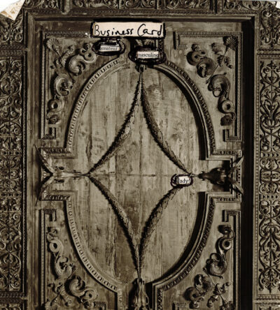 The image shows an ornate, antique-looking wooden panel or door with intricate carvings. The central design features an oval frame with diamond-shaped details inside. The panel is heavily decorated with scrollwork, floral patterns, and geometric shapes. The overall appearance is aged and weathered, giving it a vintage or historic feel. Small pieces of paper with handwritten text are attached at various points on the panel.