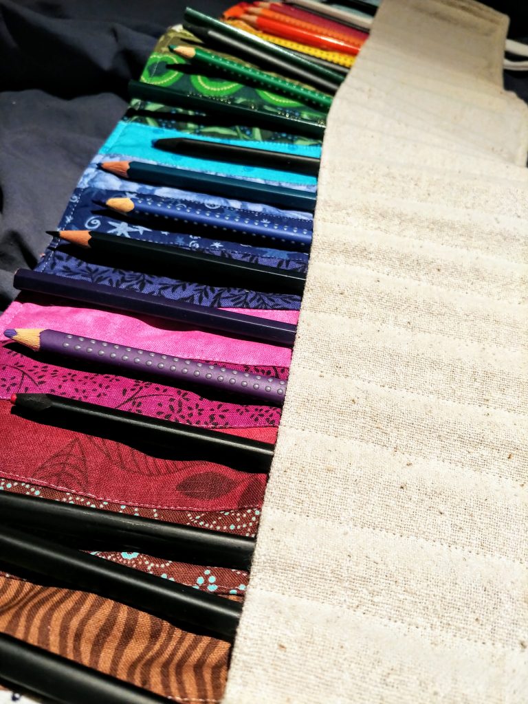 Colored Pencils arranged in canvas pockets with bright fabric behind.