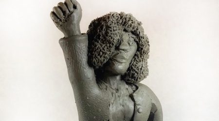 Sculpture of a Black person in a skirt suit and Afro holding their fist in a Black power salute