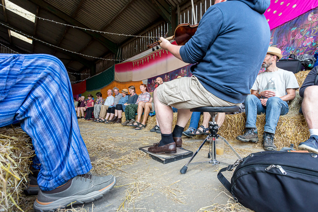 A man plays the fiddle and the podorhythm while an audience watches.
