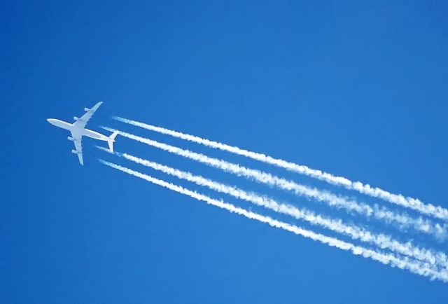 A jet plane in the sky with four contrails behind it.