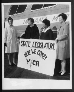 image of four women standing in front of a bus holding a sign that says state legislature here we come YWCA