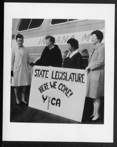 image of four women standing in front of a bus holding a sign that reads state legislature here we come YWCA