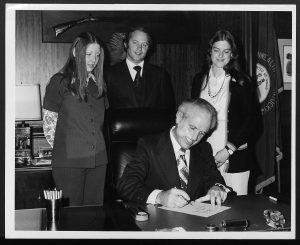 image of man signing a bill into law and two women and a man standing behind him
