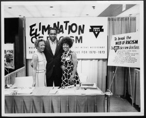 image of three people standing in front of a poster that reads "Elimination of Racism"