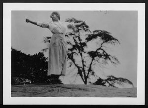 photograph of woman standing outside possibly on top of hill or mountain stretching arms wide