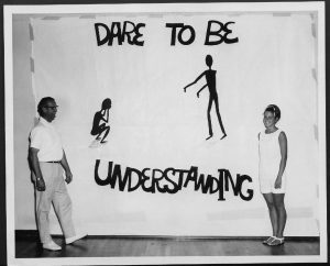 black and white photograph of a man and a woman standing in front of a banner that says dare to be understanding