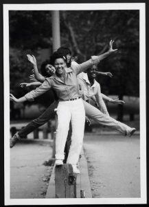 black and white photograph of women balancing on beam with various legs and arms out to either side