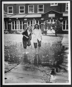 black and white photograph of two women with pants rolled up standing in a large puddle