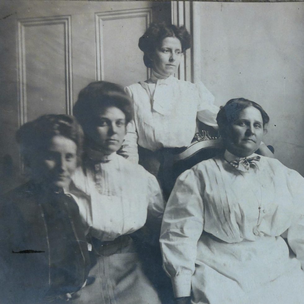 Picture of three young white women sitting or standing next to an older white woman.