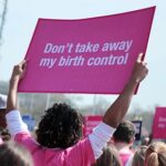 A photograph of a woman holding up a sign that reads "Don't take away my birth control" at a protest.