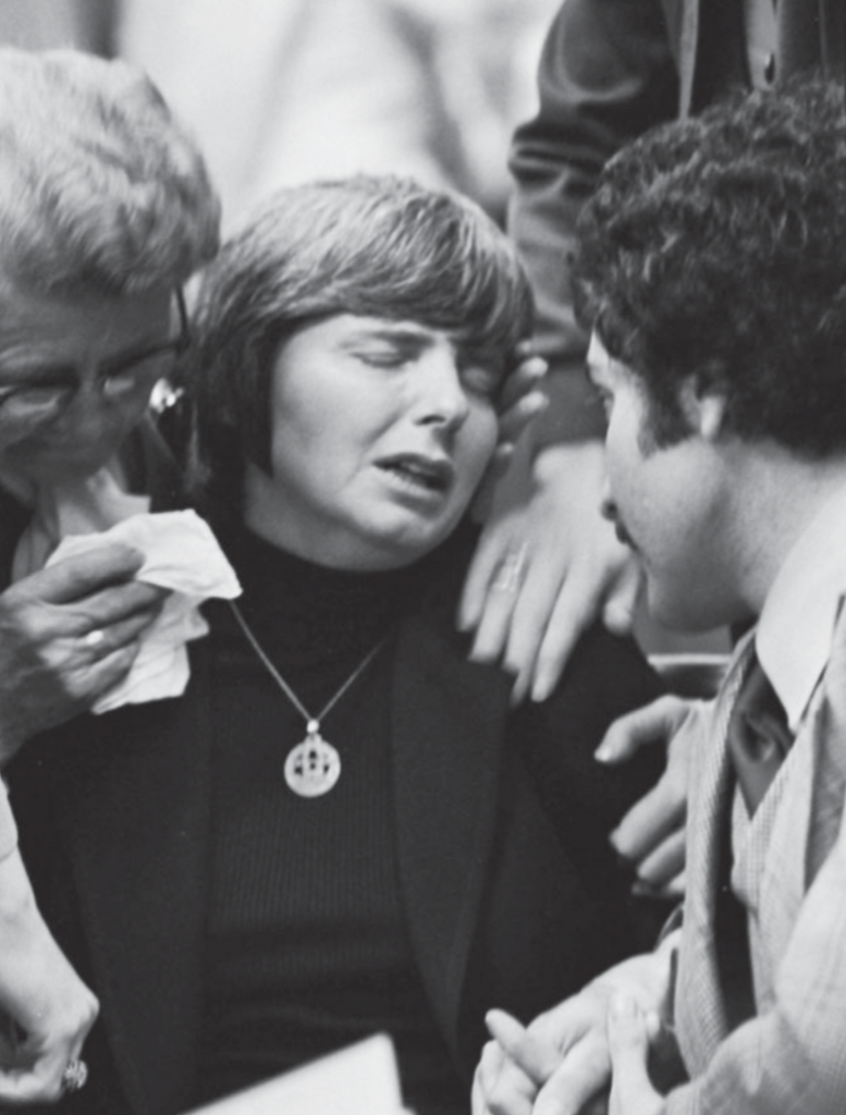An overwhelmed woman being supported by two other people