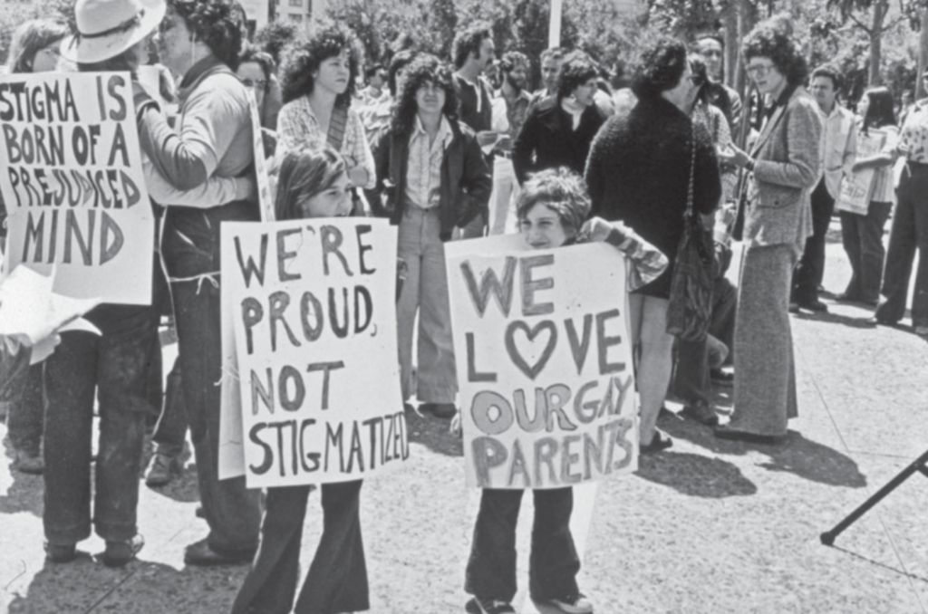 Two children at a rally hold signs that say "we're proud, not stigmatized" and "We love our gay parents"