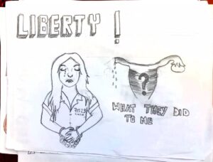 drawing showing a woman crying and in handcuffs and a question mark within a uterus, "liberty!" is written at the top of the paper and "what did they do to me?" at the bottom