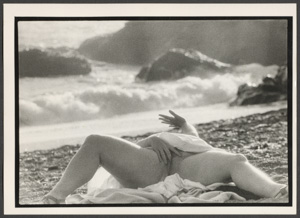 A woman laying on the beach with her legs spread, inserting her fingers into her vagina.