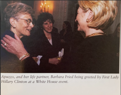 Photograph of three white women smiling and talking to each other. The included caption reads, "Apuzzo, and her life partner, Barbara Fried being greeted by First Lady Hillary Clinton at a White House event."
