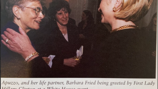 Photograph of three white women smiling and talking to each other. The included caption reads, "Apuzzo, and her life partner, Barbara Fried being greeted by First Lady Hillary Clinton at a White House event."
