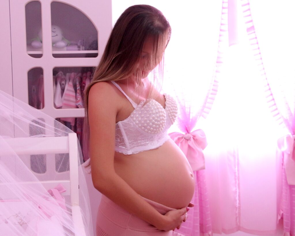 A pregnant woman with a baby's pink room as a background