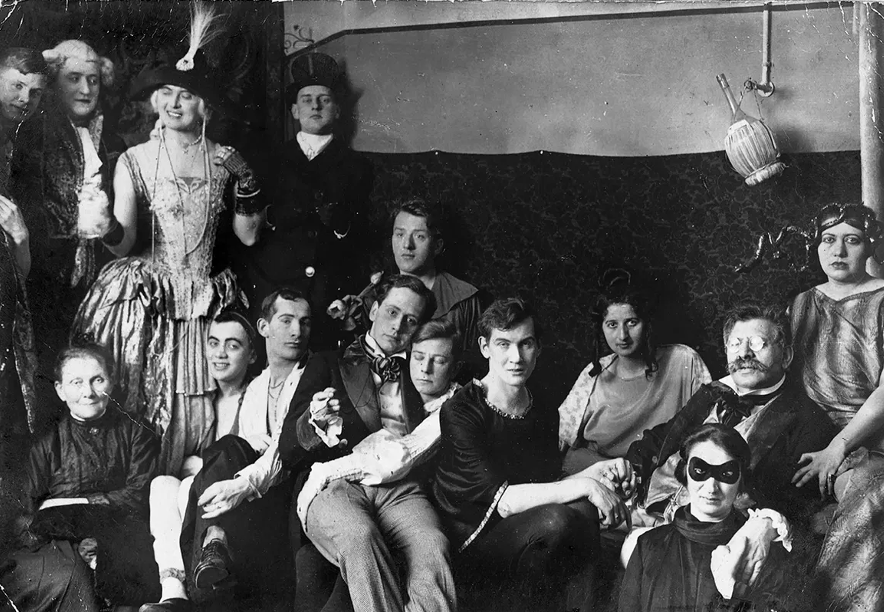 Photograph from a costume party at the Institute for Sexual Research showing Magnus Hirschfeld on the right wearing glasses and holding hands with his partner.