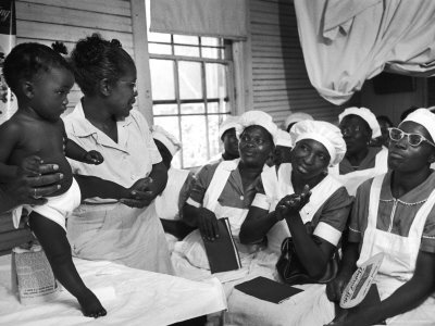 A black and white photo of a group of Black midwives learning from a mentor.