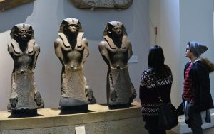 Image of two visitors observing three ancient Egyptian statues at the British Museum.