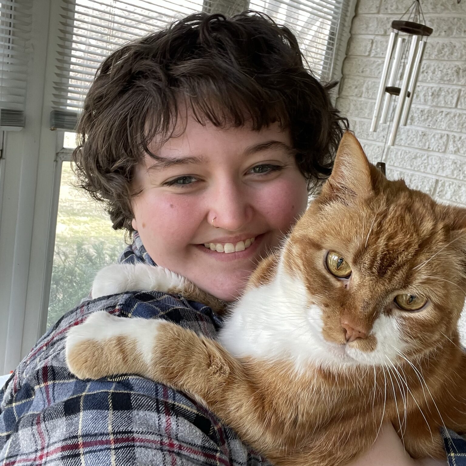 Fern Poling '25 poses with their cat, Toby, who seems to express anger with their narrowed amber eyes. 
