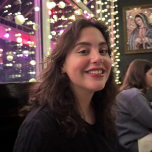 Mary smiles at the camera, with glowing circular lights and a painting of Our Lady of Guadalupe behind her.