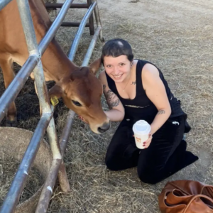 Madison kneels next to a farm animal, holding a cup of Dunkin Donuts coffee in one hand and the animal's chin in the other.