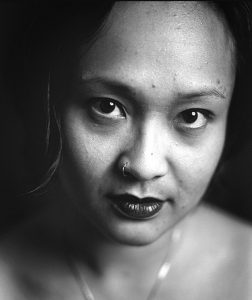 close up portrait of female identifying AAPI with a serious direct look. Portrait is b&w and makes use of shadows and light.
