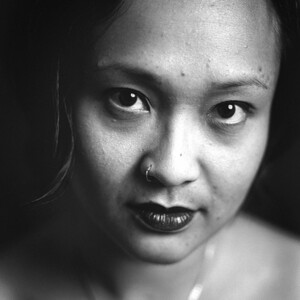 close up portrait of female identifying AAPI with a serious direct look. Portrait is b&w and makes use of shadows and light.