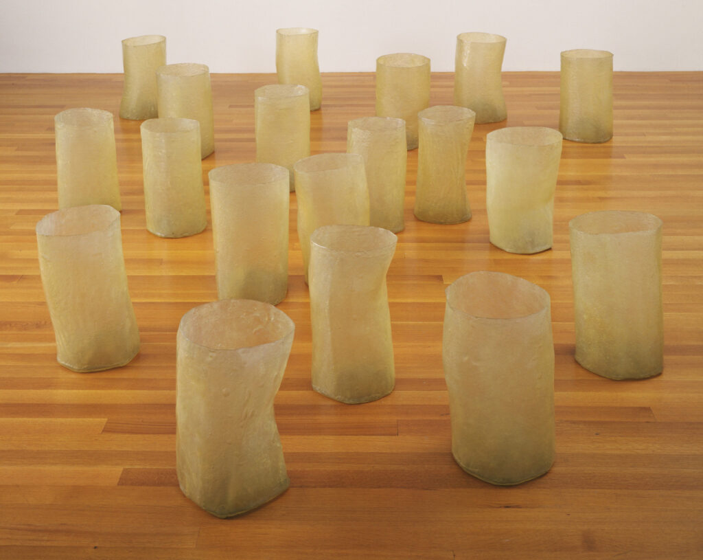 19 translucent, bucket-like forms, each approximately 20 inches tall. They are handmade and irregular rather than manufactured and hard-edged, sitting on the gallery floor