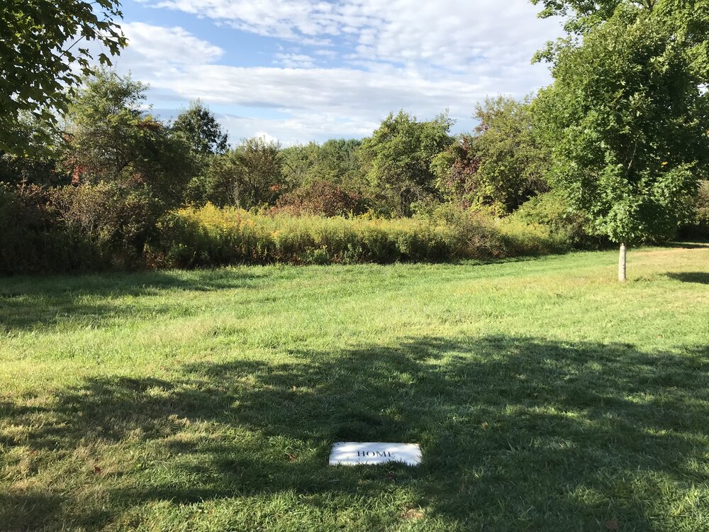 White marble stone flat against the ground with the word "HOME," in a grassy field