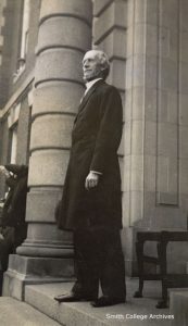 A black and white photograph of President Seelye from the side. He is wearing a long jacket and pants.