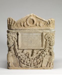 A carved stone box with images of faces on the corner and a plaque with words in the center.