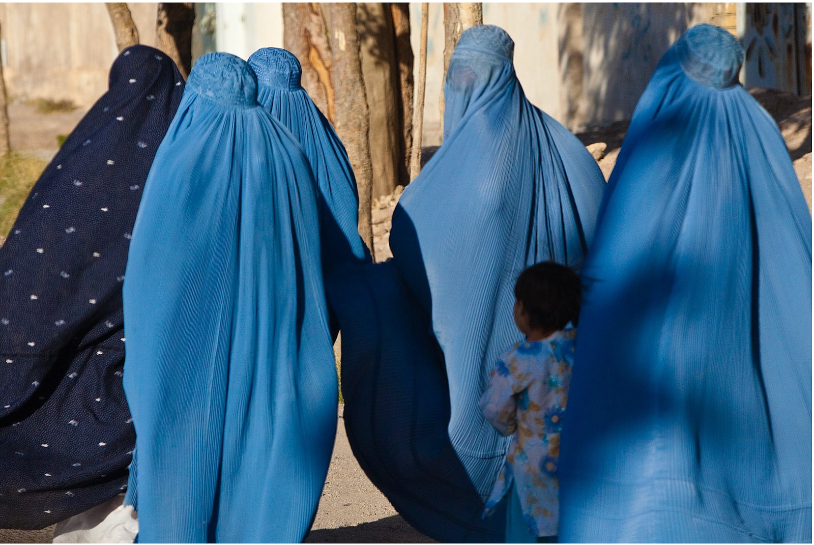 A group of women in blue burqas walking together along a city street