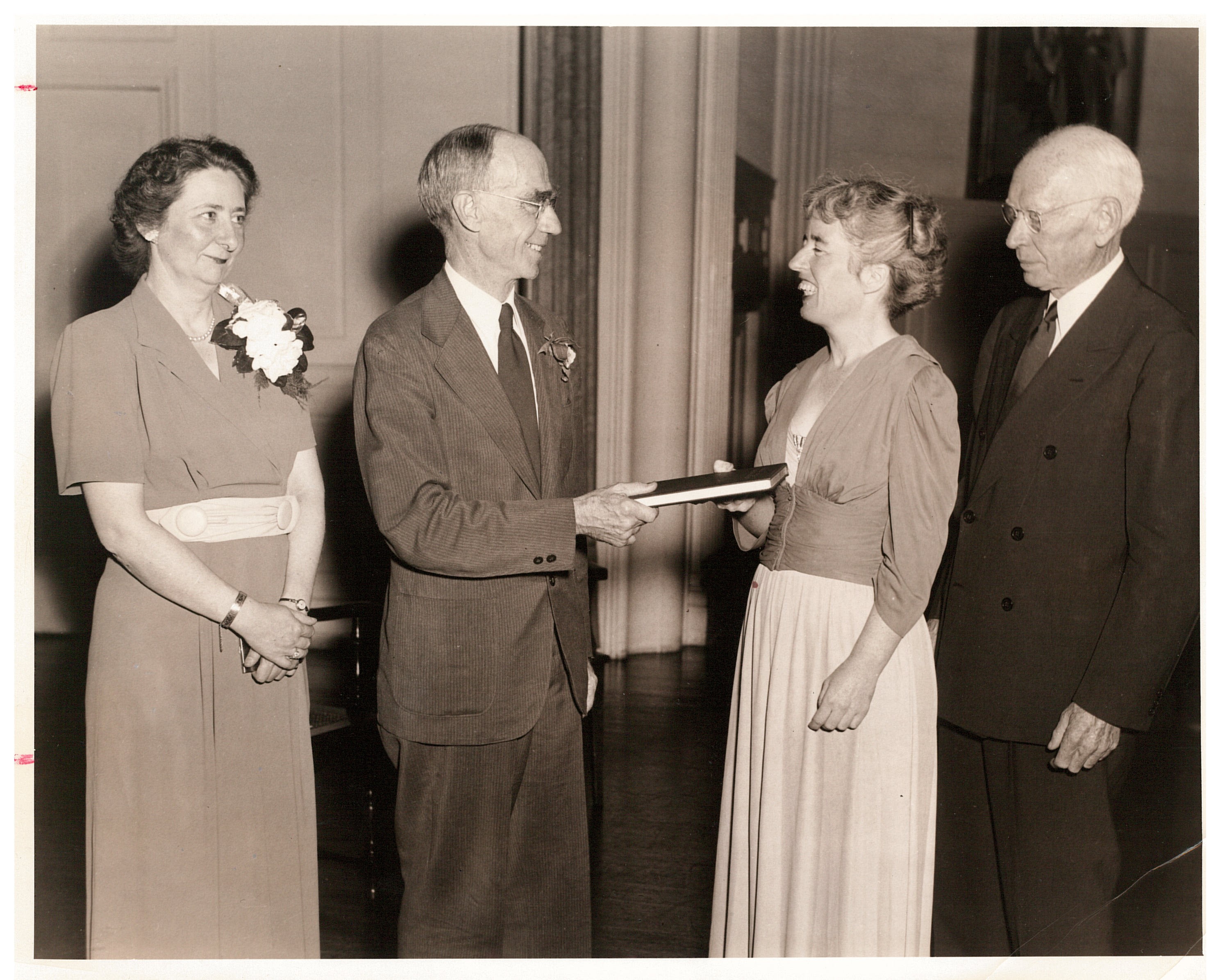 Black and white photo of four people. On the left is someone in a dress, then Everett Kimball handing a diploma to another person in a dress.