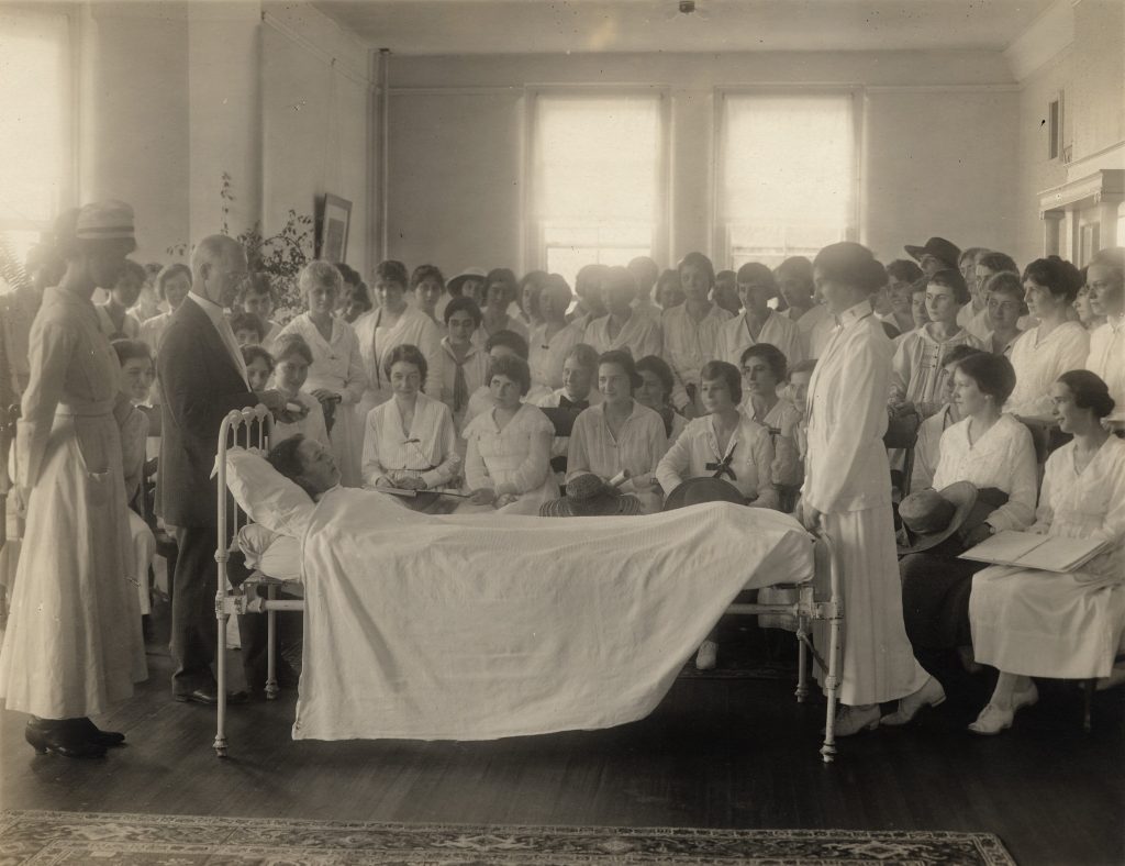 Black and white photo of a class around bed with patient