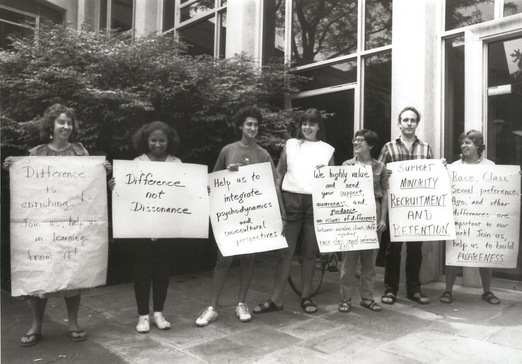 Black and white photo of an interracial group of protesters. One sign says "Difference not Dissonance"