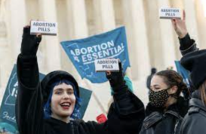 This photograph shows abortion activists holding up boxes that say abortion pills and a sign that says abortion is essential. 