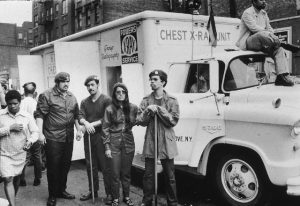 Black and white photograph of four members of the young lords standing in front of a white truck labeled "Chest X-Ray."