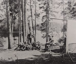 A group of campers and staffman standing on a campsite. 