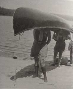 Two girls carry a canoe on their heads.